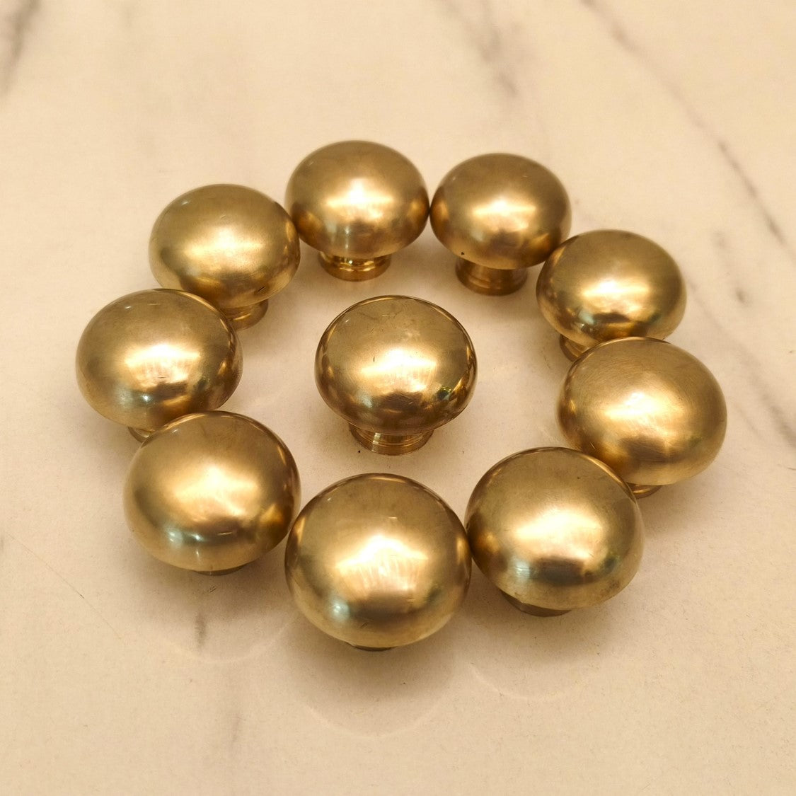Set of handmade burnished brass cabinet knobs arranged in a circle on white marble