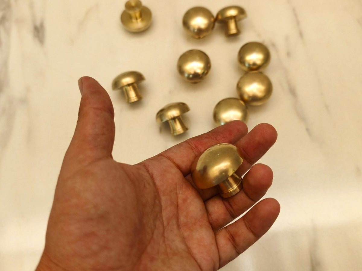 Burnished brass cabinet knob held in hand to show size and mushroom shape